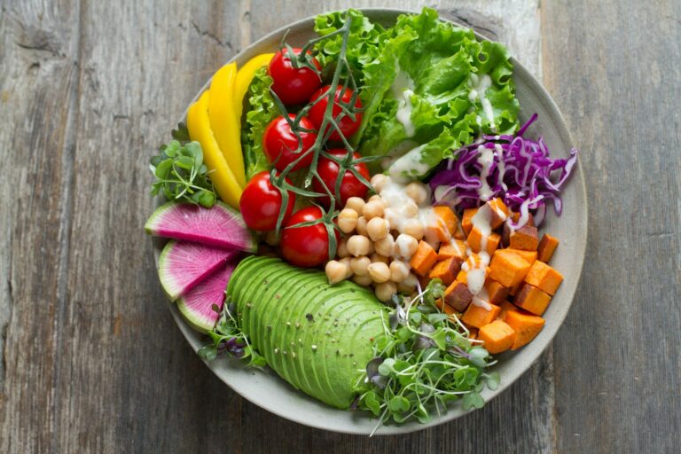 Bol de ensalada con verduras de distintos colores, aguacate y hojas verdes