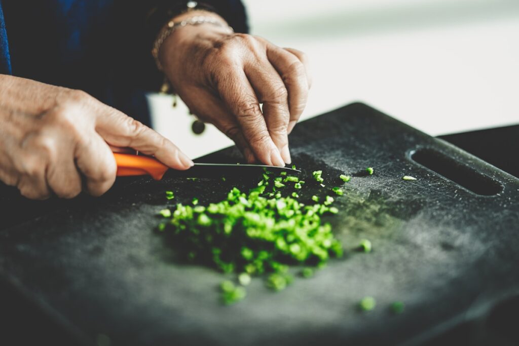 Manos cortando verduras sobre una tabla de cocina